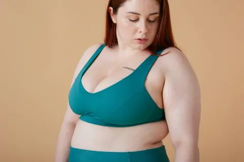 wegovy injection sites | woman in green sports bra against neutral background looking down