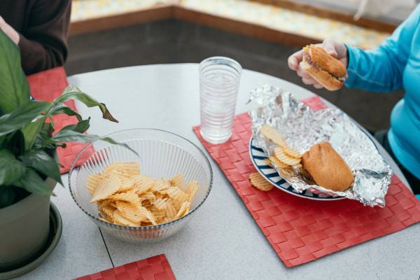 what causes obesity | people sat at table with burgers on plates and chip in bowl
