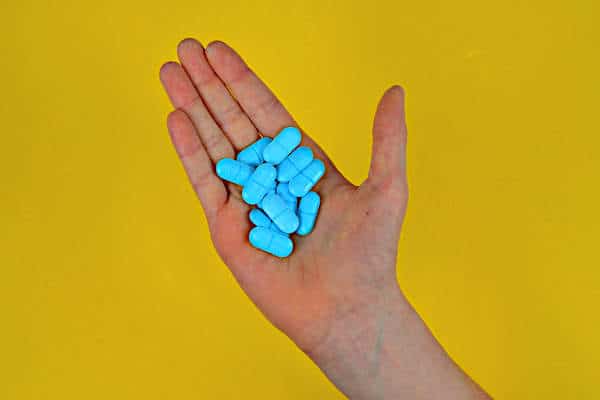 Orlistat Side Effects | Hand holding pills on yellow background