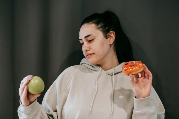 foods to avoid mounjaro | woman in grey jumper with apple in one hand and donut in another
