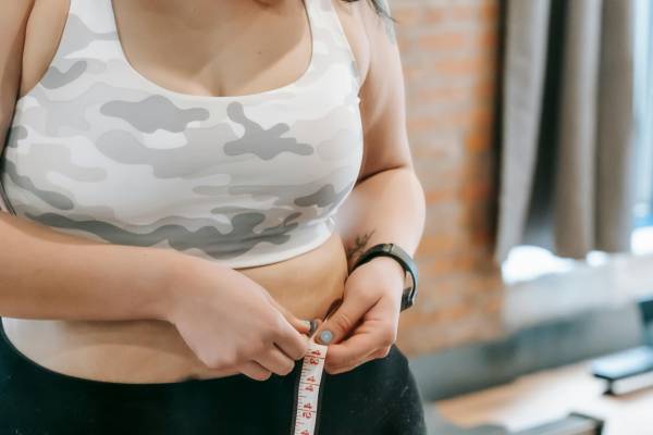 is obesity a disease? | woman in sports bra measuring stomach with measuring tape