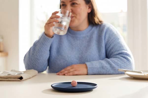 Managing foundayo side effects - lady drinking water with foundayo tablet on the table.